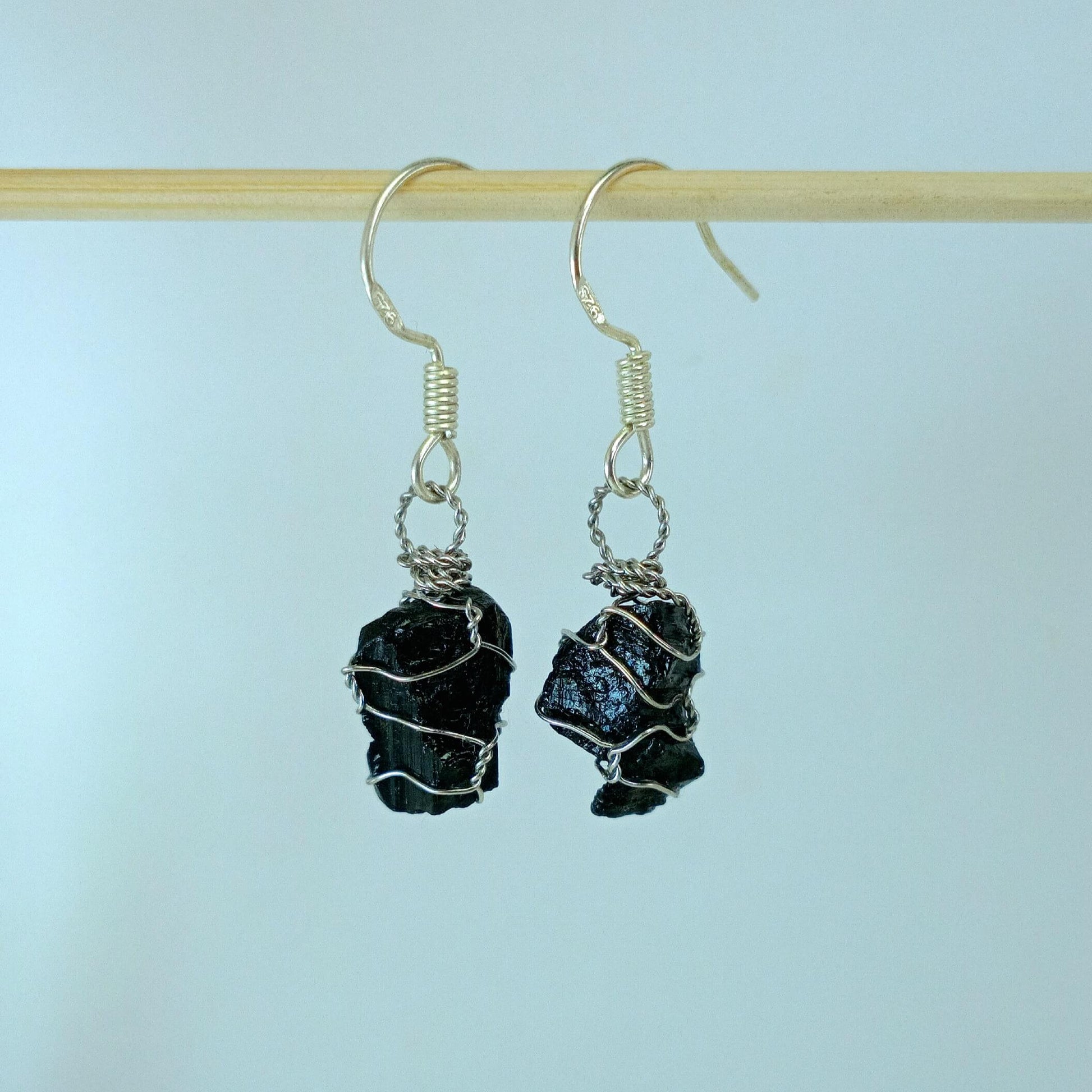 Black tourmaline stone earrings with stainless steel wire wrapping on a light blue background