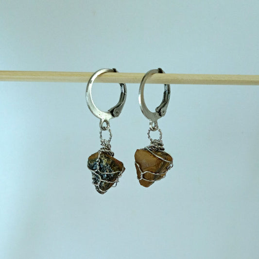 Pair of stainless steel hoop earrings with Tiger eye stone drops on a light blue background