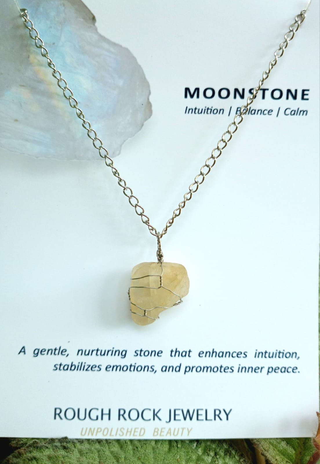 Necklace with a rough stone pendant on a natural background, featuring text about moonstone properties.